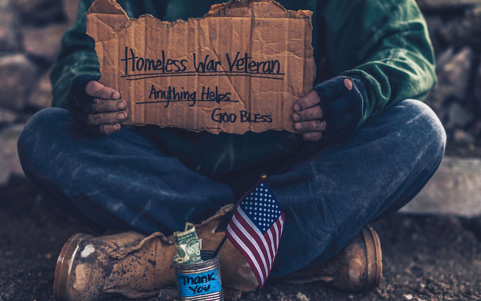Man holding sigh saying "Homeless War Veteran Anything Helps God Bless" with American Flag