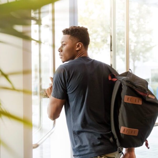 A young man with a backpack is pushing open a door